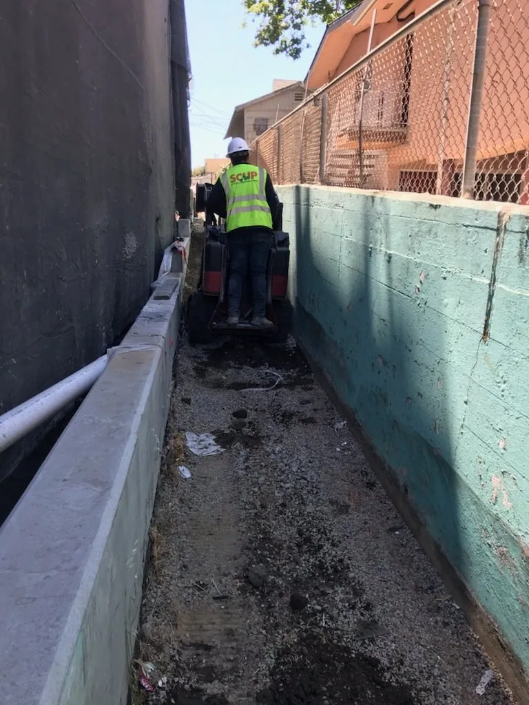 SCUP worker in a branded hi-vis vest operating a motorized wheelbarrow in a narrow trench