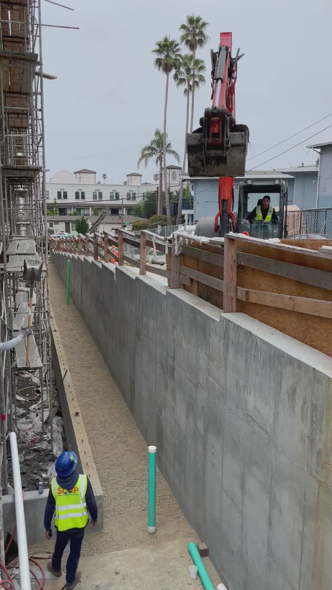 SCUP crew member and excavator lowering soil into a shored trench between concrete walls